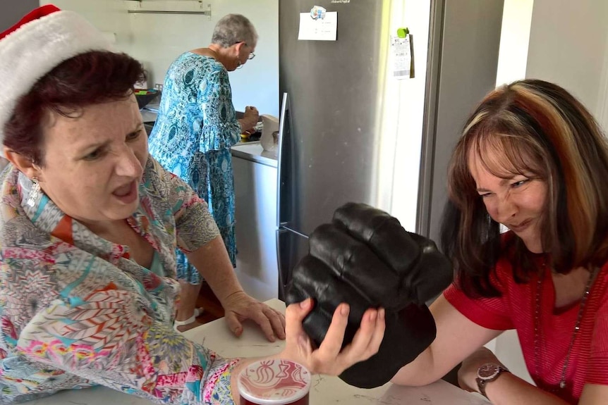 Madonna wearing a big fist faces her sister-in-law as she tries to grab it on a kitchen counter.