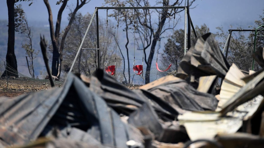 Burnt remains of a house destroyed in a bushfire, with child's swing seat in background, at Kabra, near Gracemere.