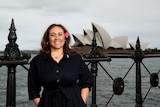 A top football executive stands at a railing with a flower in her hair and Sydney Opera House in the background.