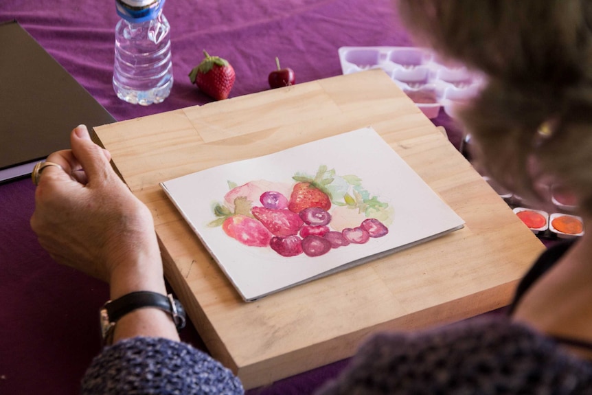 An artist paints a collection of fruit.
