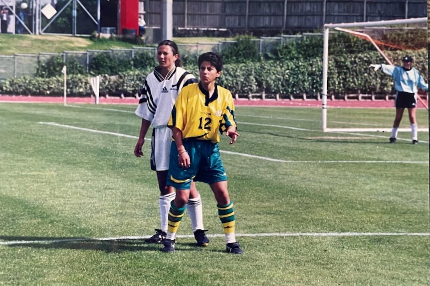 Two soccer players, one wearing yellow and green and the other wearing black and white, stand on the pitch during a game