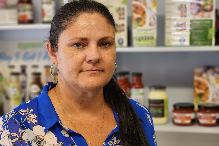 Una mujer con un traje floral azul se para frente a los estantes de productos alimenticios.