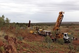 Outcropping ironstone rock with spinifex, stunted trees and exploration drill rig in the West Australian outback