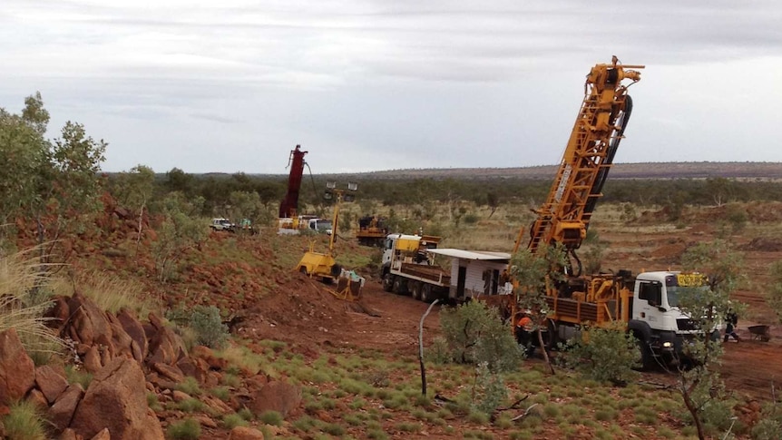 Outcropping ironstone rock with spinifex, stunted trees and exploration drill rig in the West Australian outback