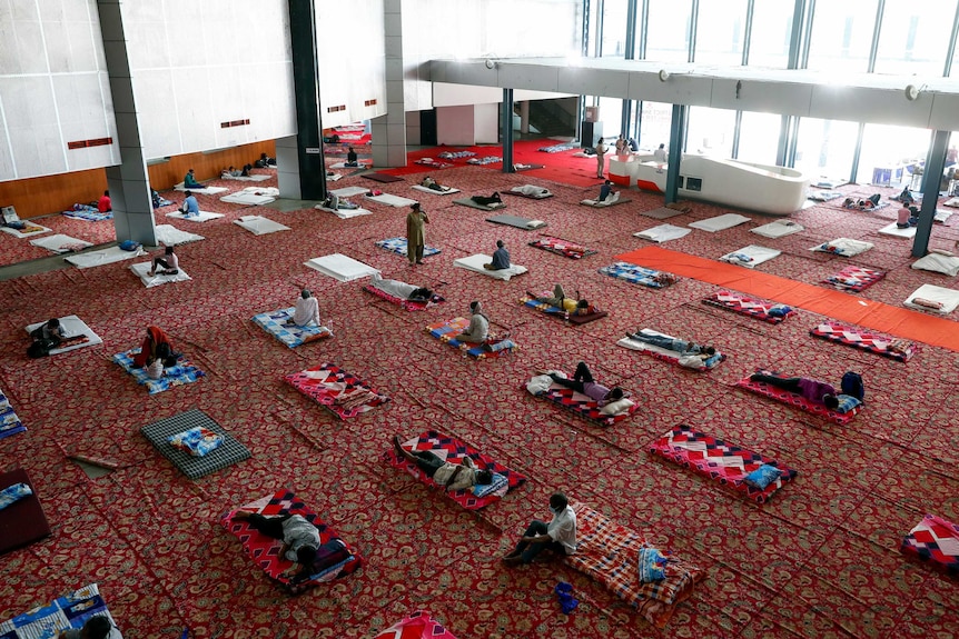 Migrant workers and homeless people rest inside a sports complex turned into a shelter
