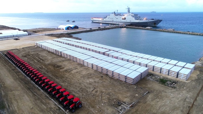 The port in Tonga with a naval ship in background and a dock full of tractors and flat pack mobile homes