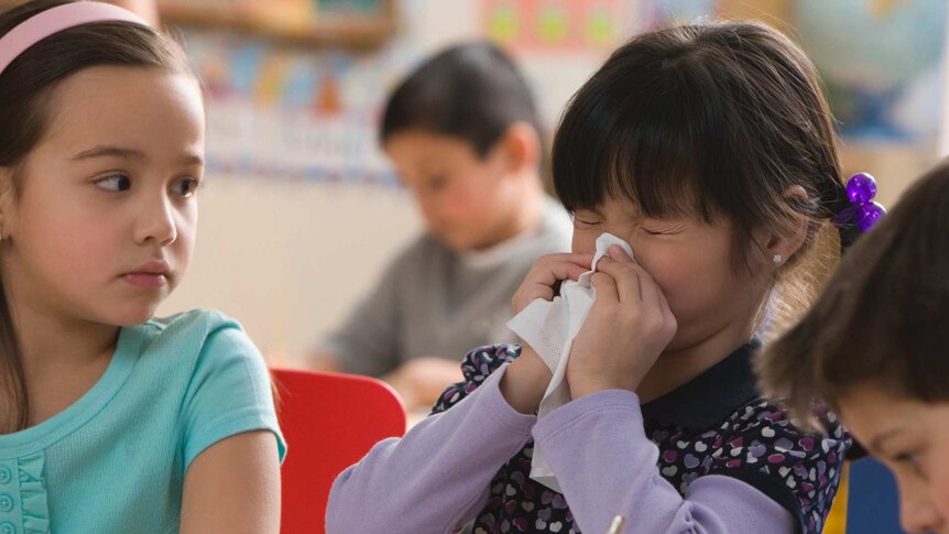 A girl is blowing her nose while sitting in between two classmates