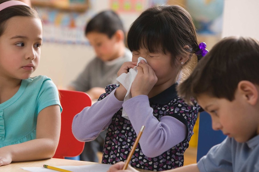 A girl is blowing her nose while sitting in between two classmates