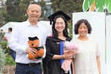Young lady wearing graduation gown pose for a photo with her parents