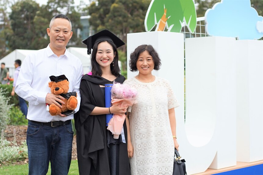 Young lady wearing graduation gown pose for a photo with her parents