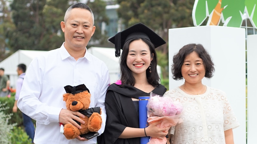 Young lady wearing graduation gown pose for a photo with her parents