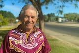 Head and shoulder mid shot portrait of an indigenous man in a maroons supporter shirt alongside a road