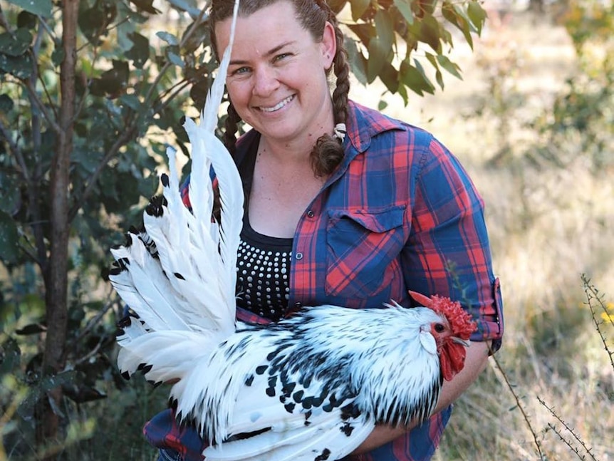 A smiling woman holds a large white chicken.