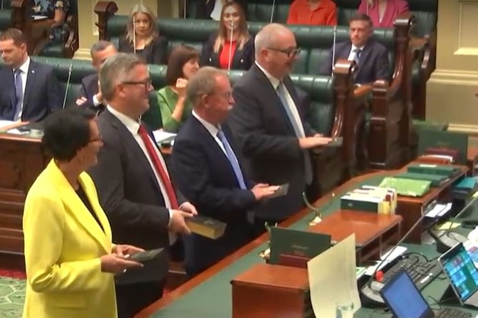 Une femme portant une veste jaune et trois hommes portant des costumes sombres se tiennent à une table au parlement