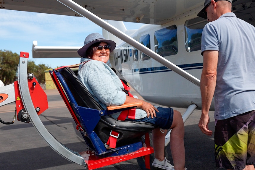 Woman strapped into mechanical chair at door of small plane.