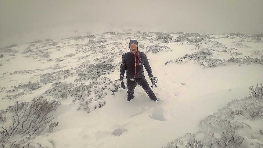 A man in a spray jacket knee deep in snow on a mountain.