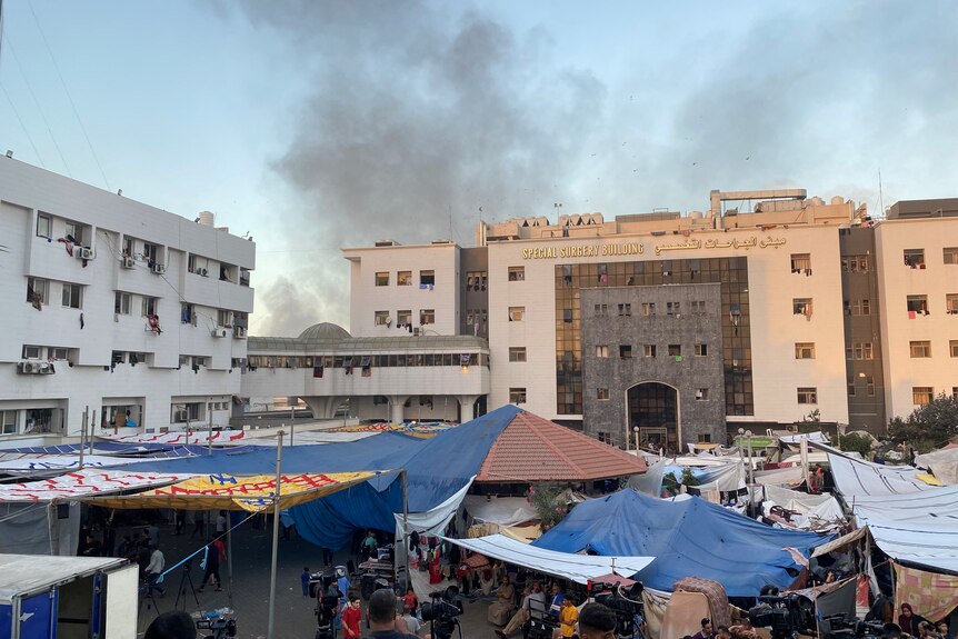 smoke rises above hospital building, while in the foreground makeshift tents can be seen