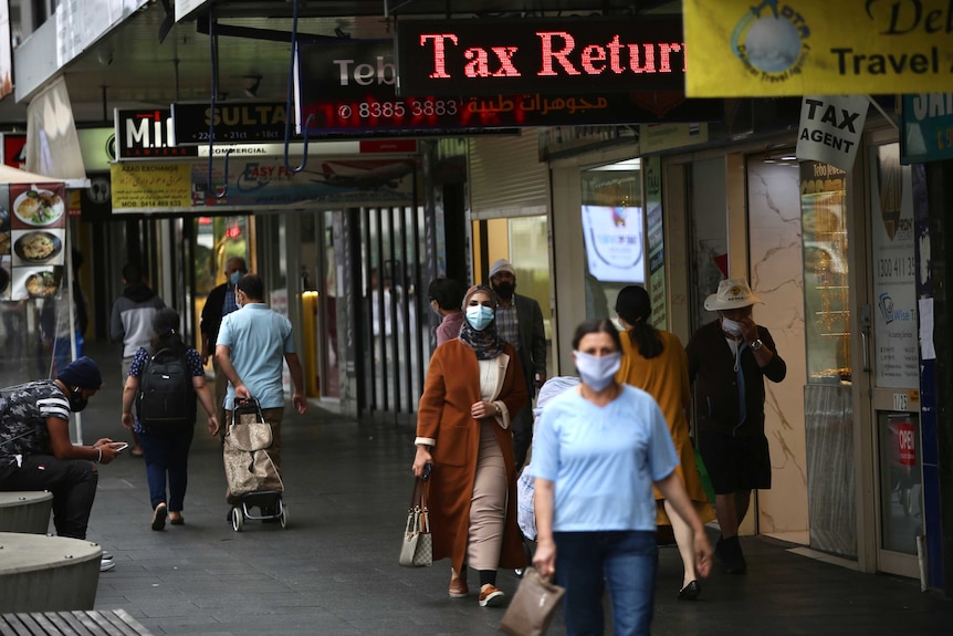 People wearing masks walk along the path in a strip mall in Auburn. There are a number of shop signs