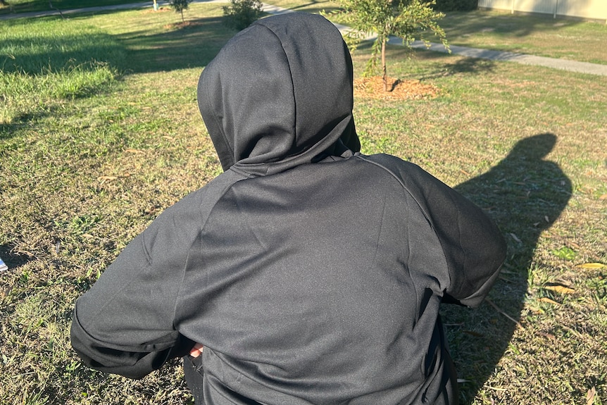 An unidentifiable person in a black hoodie sits in a field.