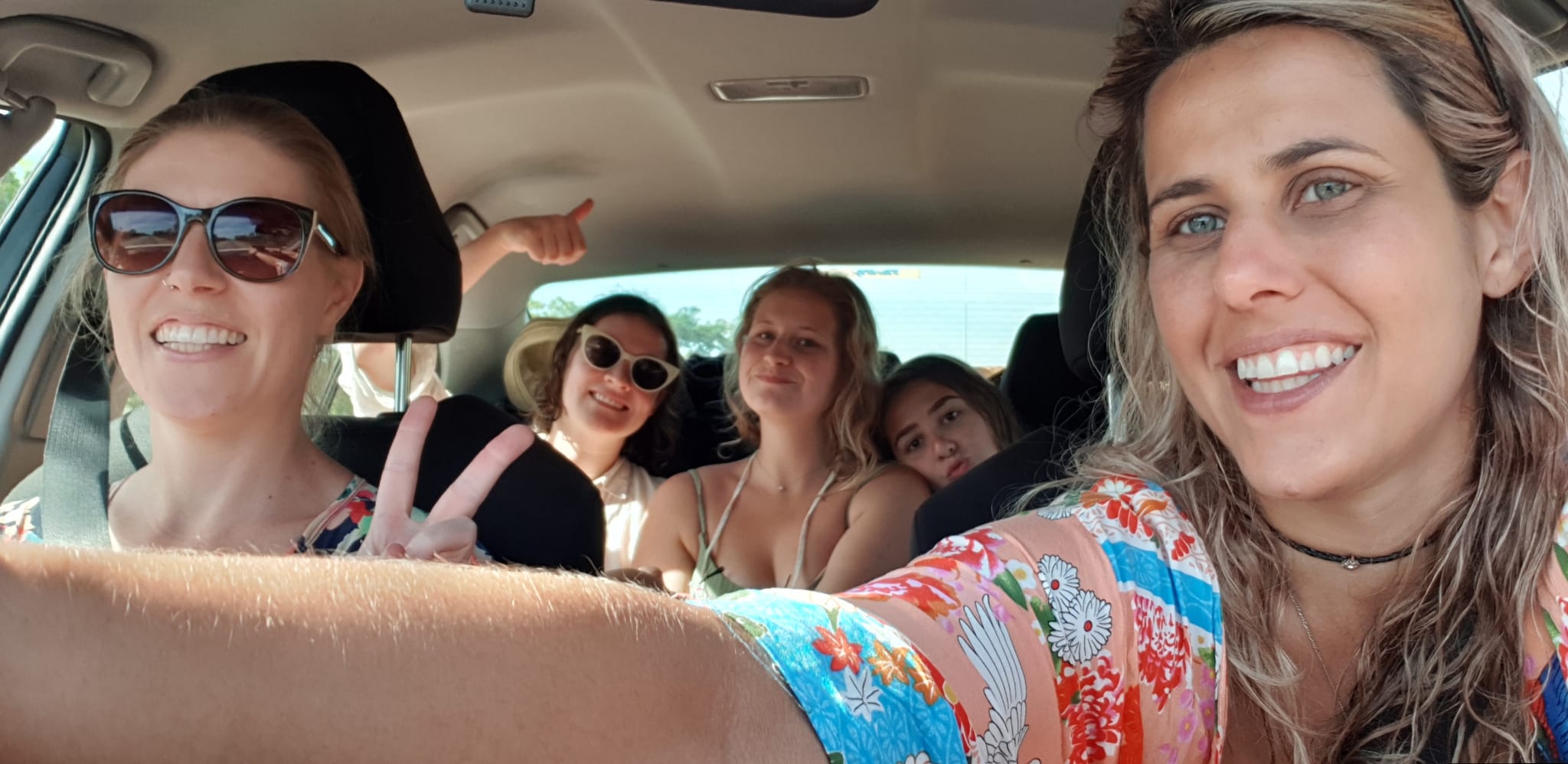 Five women smile and pose for a selfie inside a hire car.