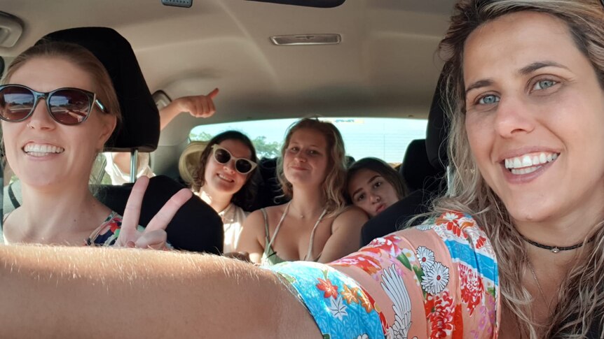 Five women smile and pose for a selfie inside a hire car.