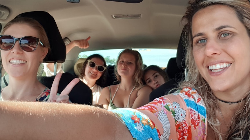 Five women smile and pose for a selfie inside a rental car.