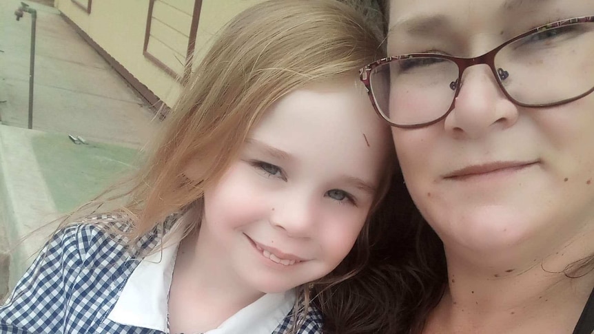 A close up of a mother with her young daughter. The girl is wearing a school uniform.