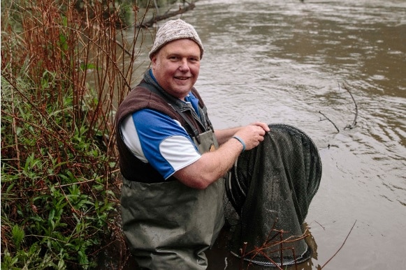 man holds fish near river