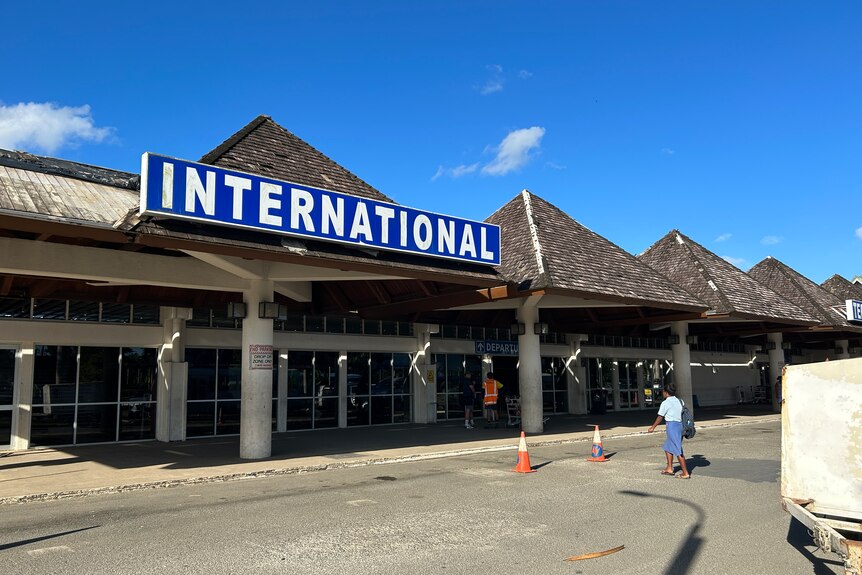 A woman walks towards an airport entry with a sign saying 'international'.