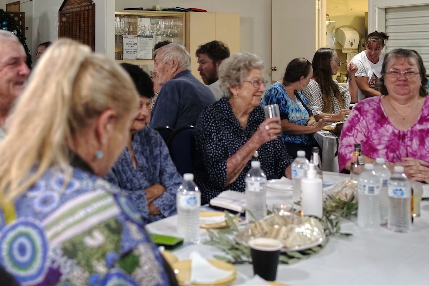 A group of people sit around a table with food on it, smiling. 