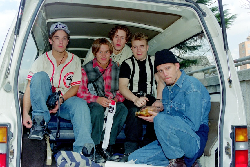 Five young men dressed casually sitting in the back of a car