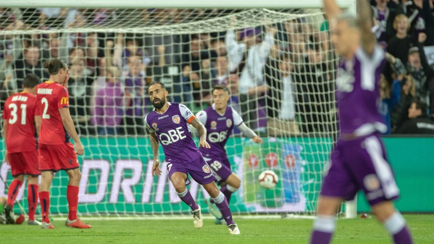 A football player wheels away after scoring a goal as a teammate in the foreground raises his arms in celebration