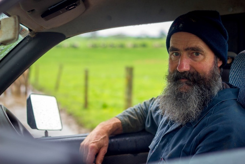 A dairy farmer sitting in a car on his farm wearing a blue beanie