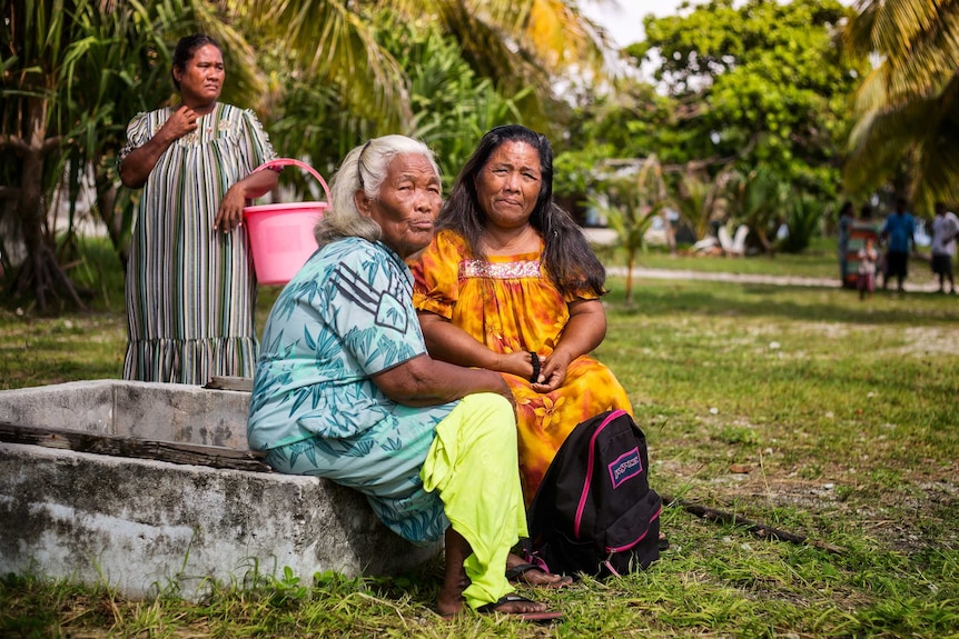 Two women sit together under the palm trees of Enewetak Atoll.