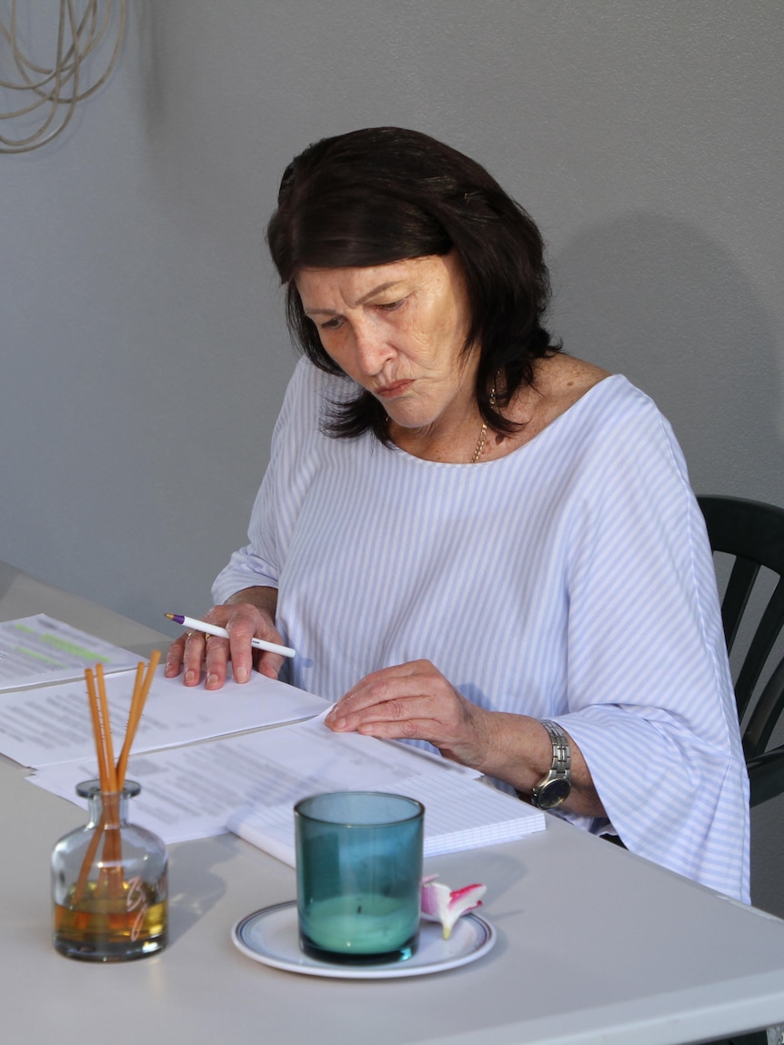 A woman sits at a table and looks at paperwork.
