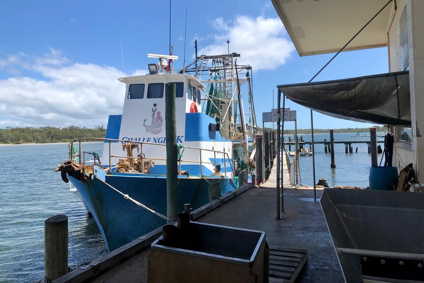 A blue and white trawler is docked at a jetty.