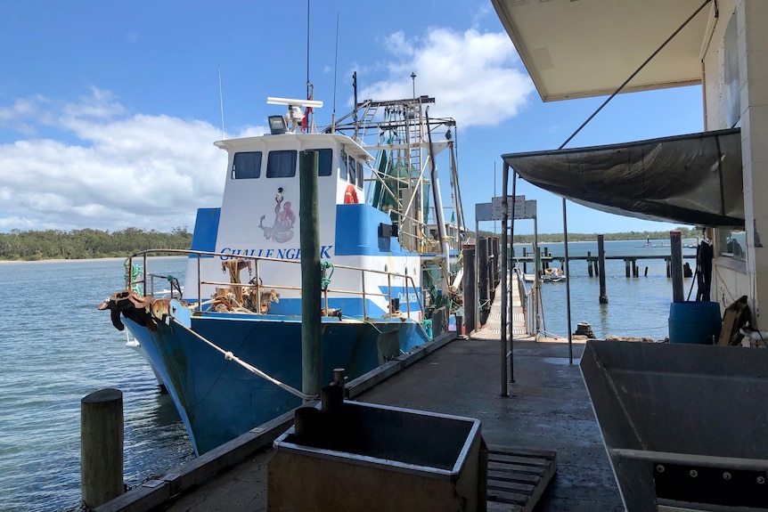 A blue and white trawler is docked at a jetty.