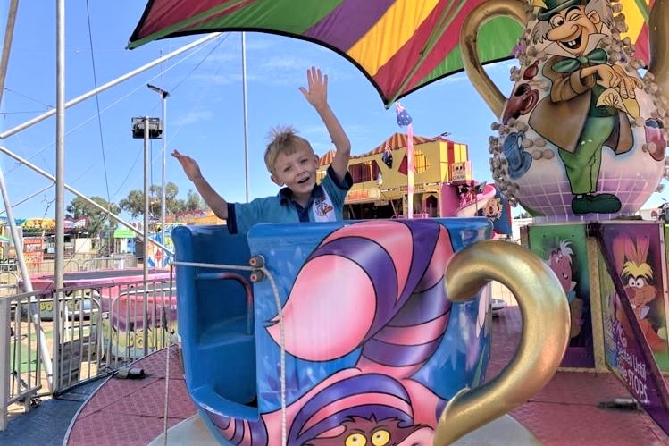 boy in school uniform takes a merry-go-round ride in a teacup 