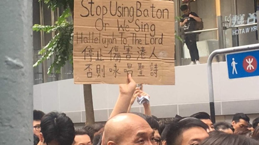 A protester in Hong Kong holds a sign warning police they will sing a hymn.
