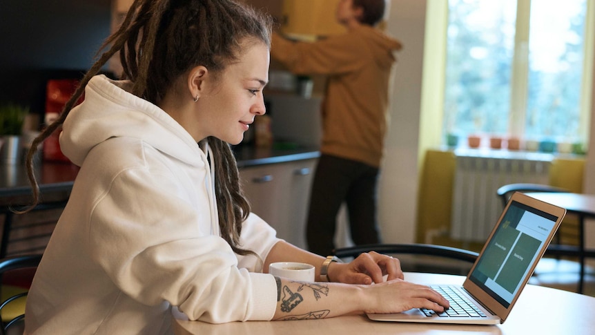 Side view of woman on her laptop at home with man in the background for story on starting a new job while working from home