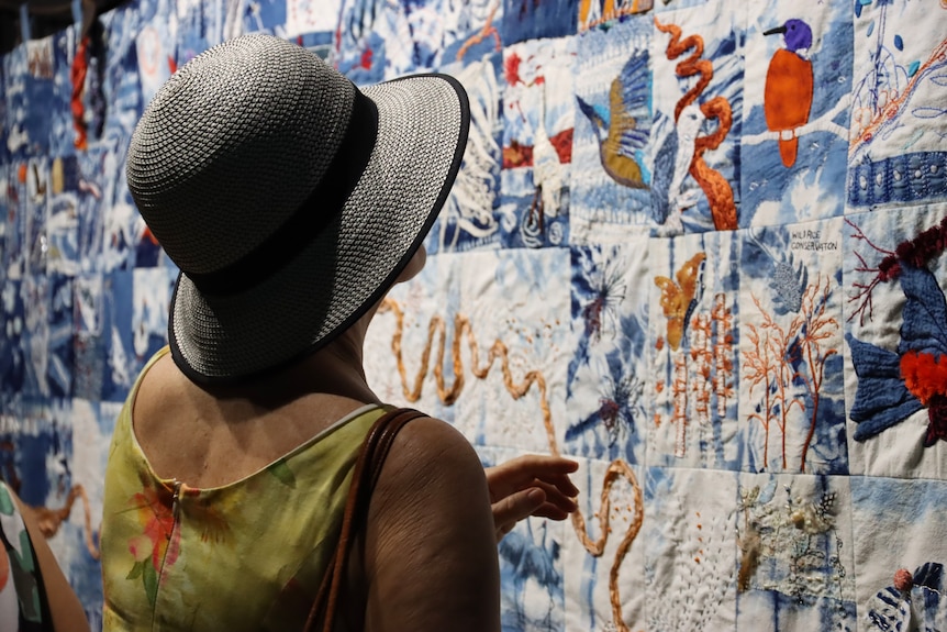 A lady with a hat looks closely at the community quilt.