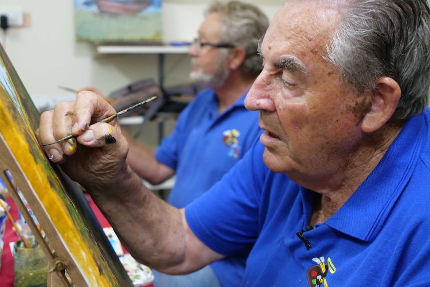 A close up of an older man painting on a canvas.