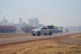 A police car is parked in front of two fire trucks and a truck carrying a water tank on the side of the road.