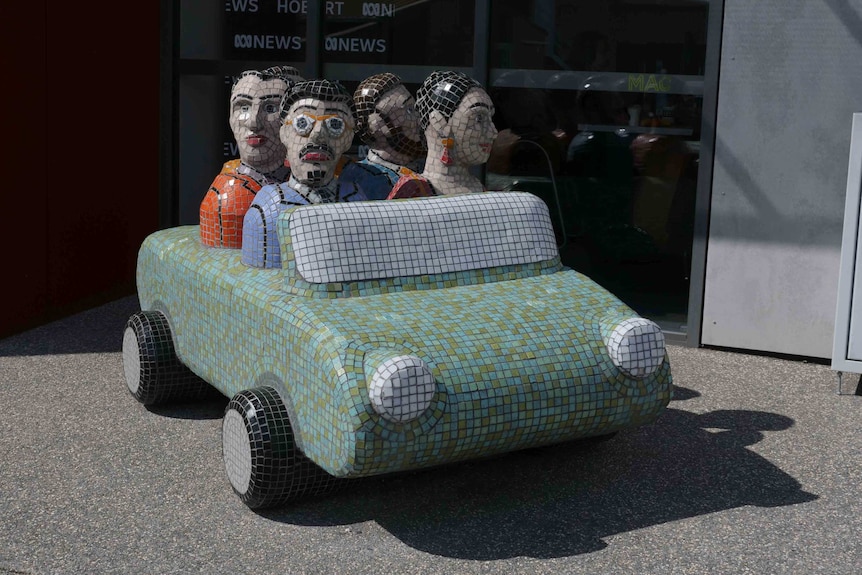A mosaic green car with five figures sitting in it.
