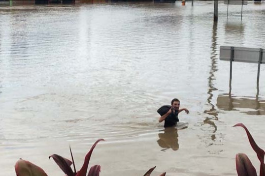 Ingham resident Stephen Munro wading waist-deep through floodwaters on Townsville Road.