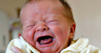 A red-faced newborn baby screams with its eyes closed.