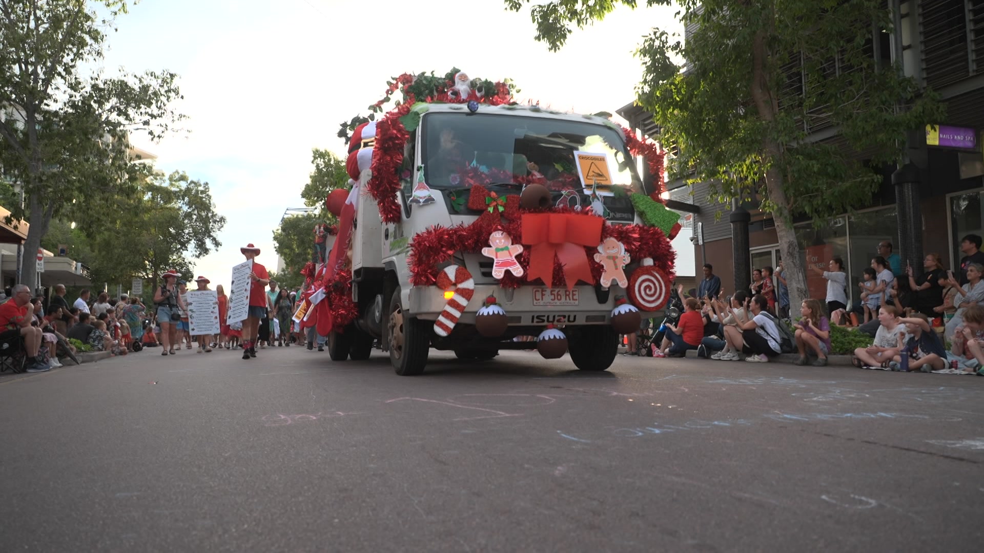 A truck covered in Christmas decorations driving down a street in the Darwin CBD, as spectators watch.
