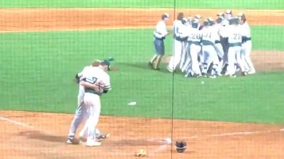 Two baseball players hug in the foreground whilst a group celebrate in the background