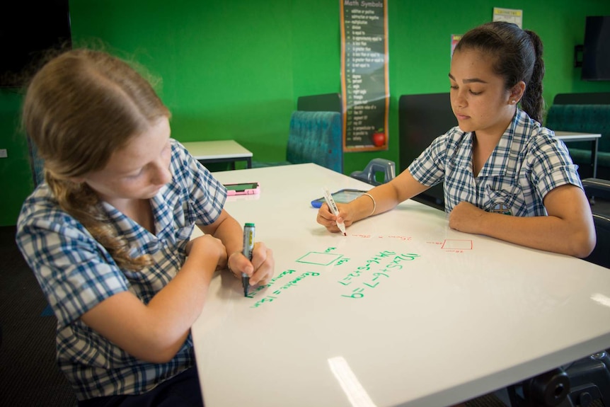 School students write on tabletops with whiteboard markers.