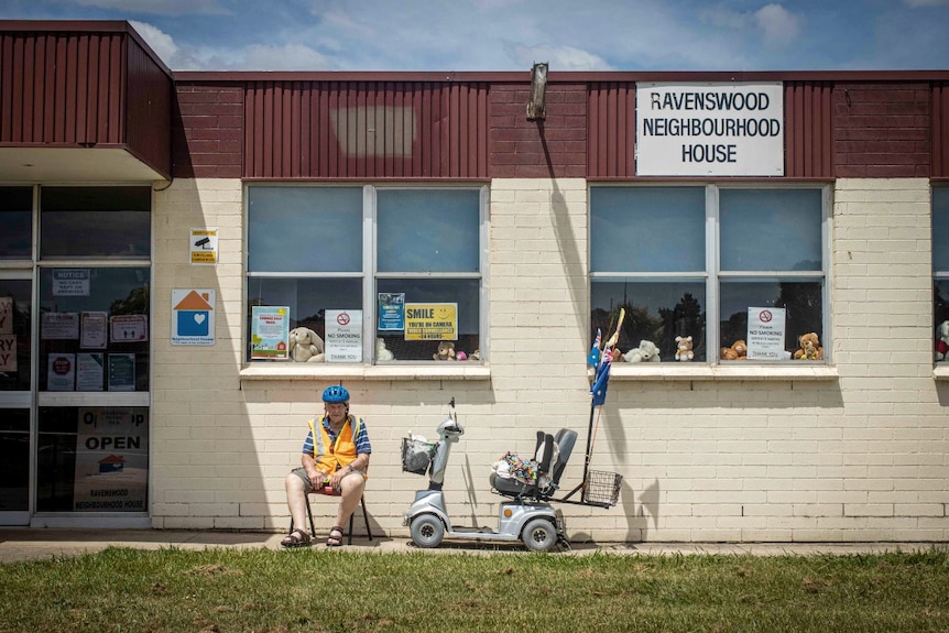 An elderly man sits next to his motorised chair outside a building